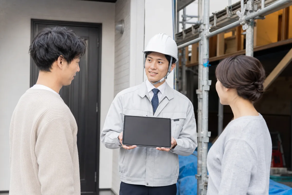 施主と改修現場の間でタブレットを持ち調整する建設業の営業担当者
