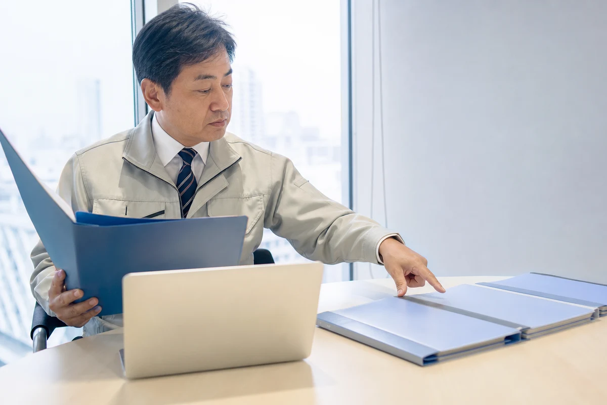 建設業の営業で公共工事入札に向けた書類を順に確認する建設会社の担当者